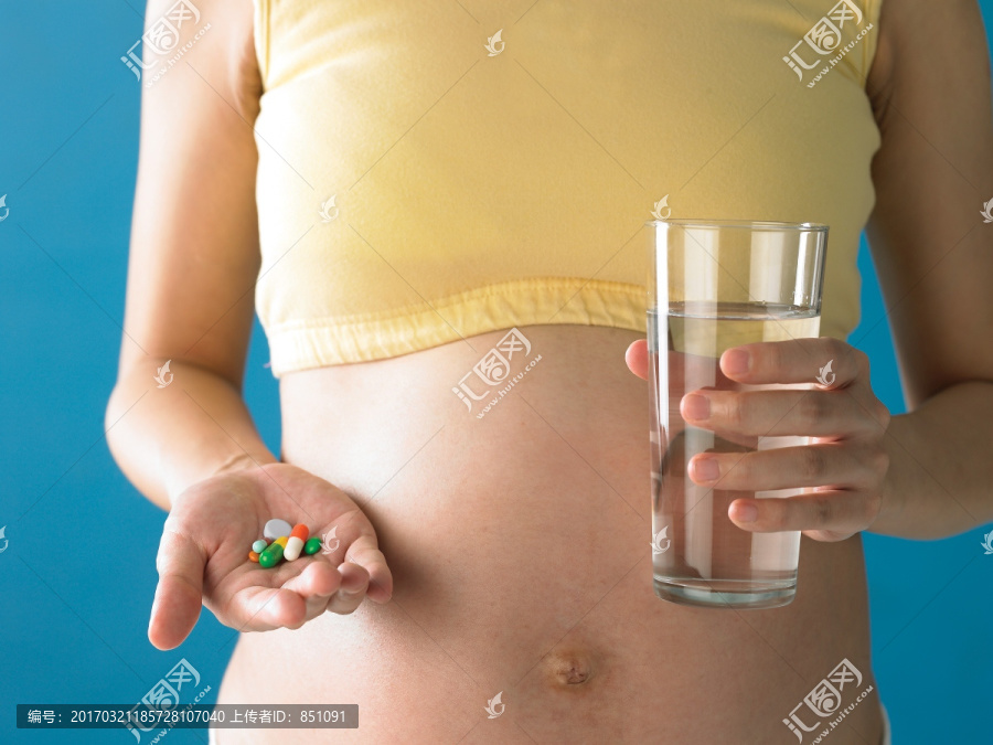 拿着一颗胶囊和一杯水的孕妇