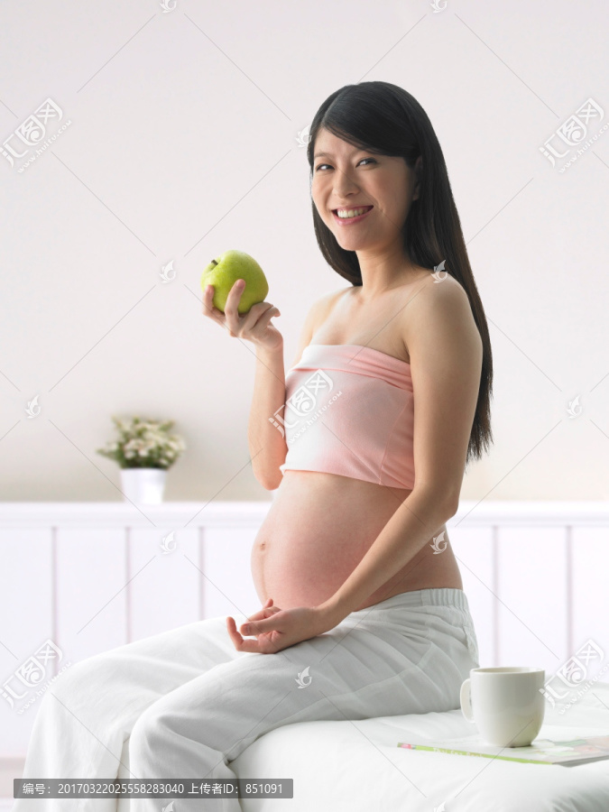 坐在床上拿着一个苹果的孕妇