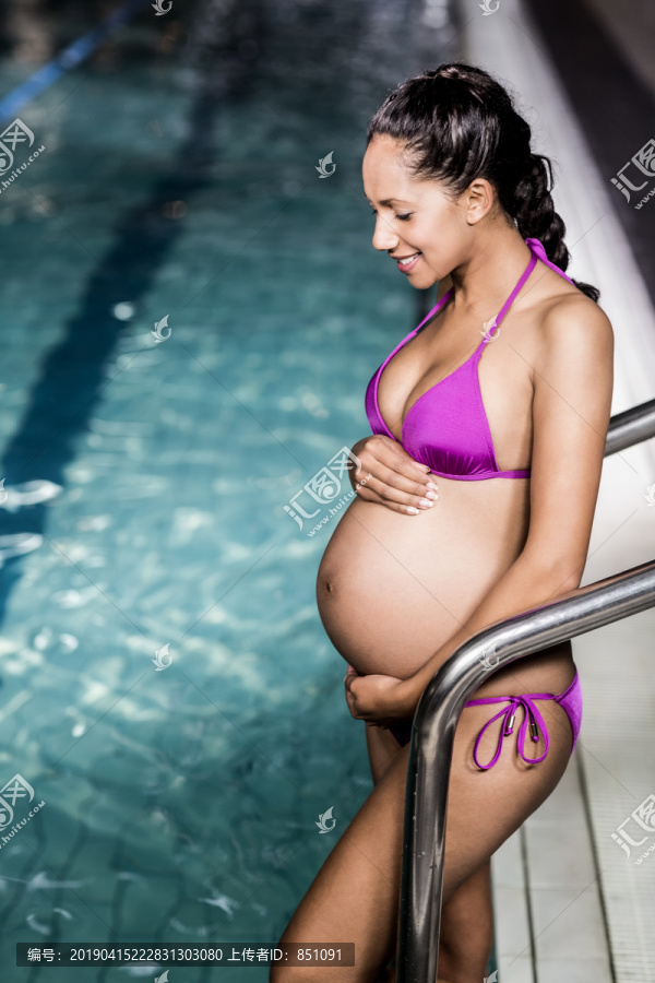 游泳池里微笑着的孕妇摸着肚子