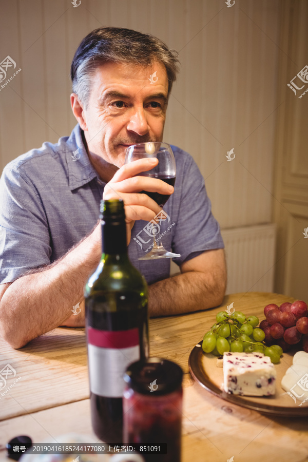 成熟的男人坐在桌旁品尝红酒