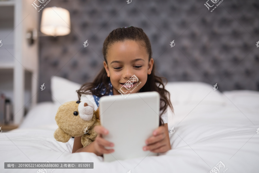 躺在床上拿着平板电脑的小女孩