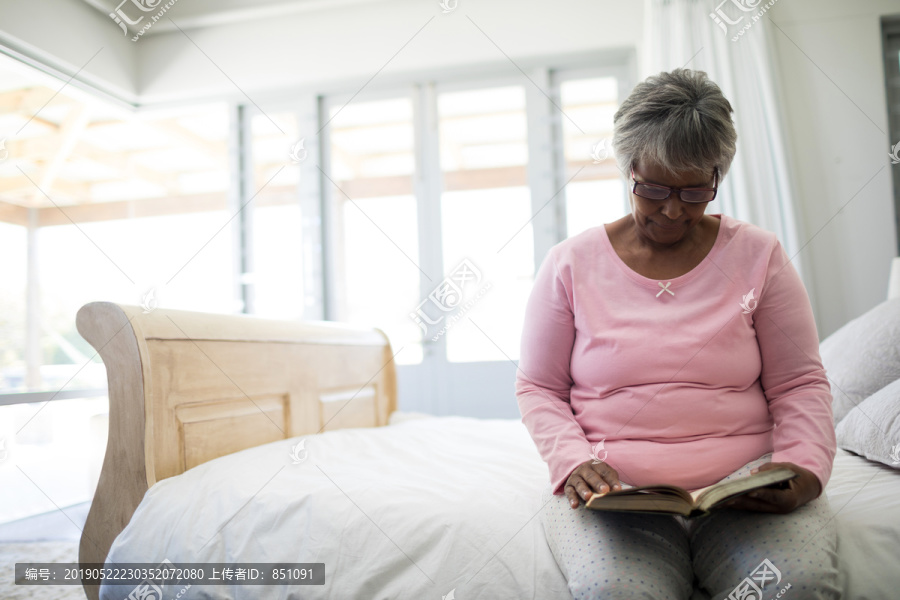 老年妇女坐在家里卧室的床上看书