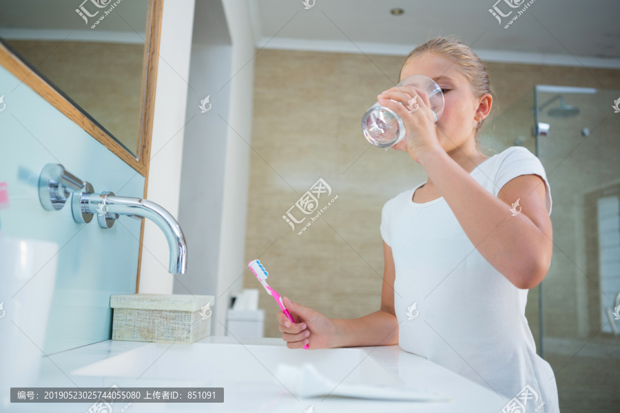 女孩拿着牙刷在浴室水槽边喝水