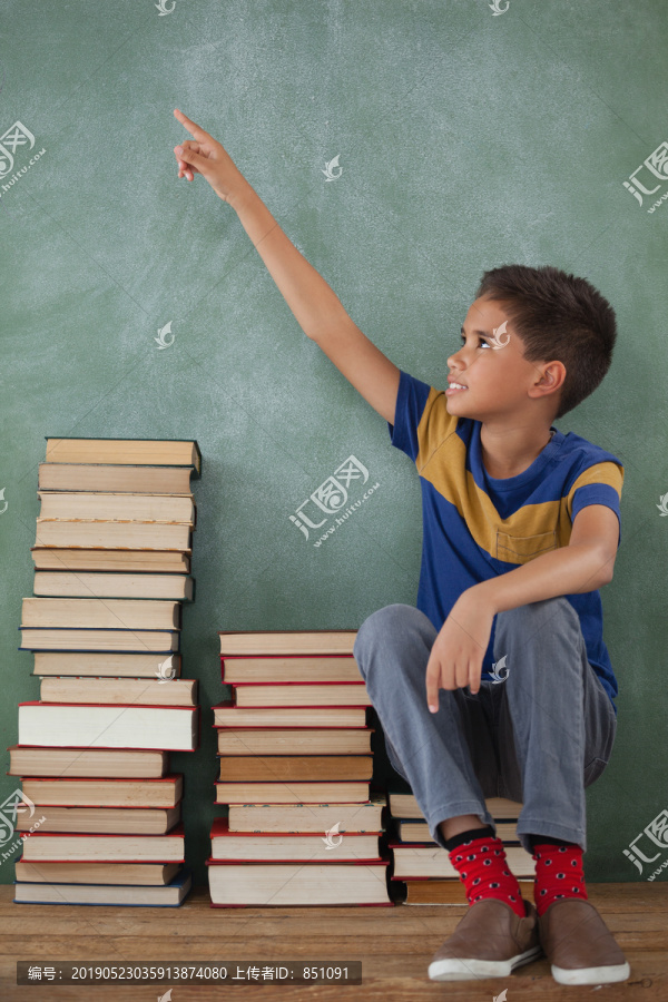 学生坐在教室黑板前的一堆书上