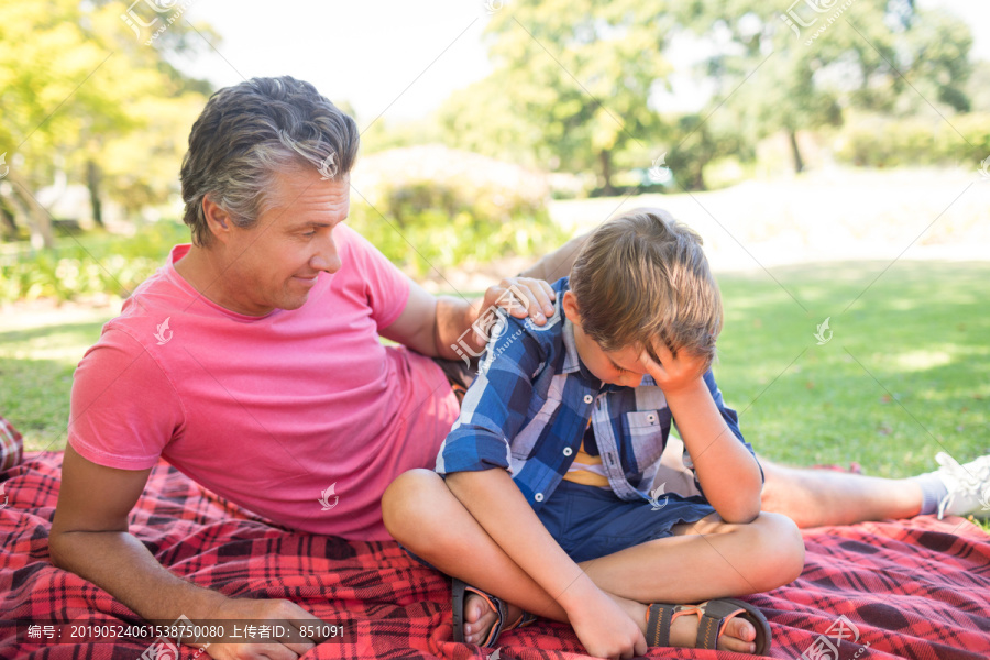 父子俩躺在公园里的野餐毯上
