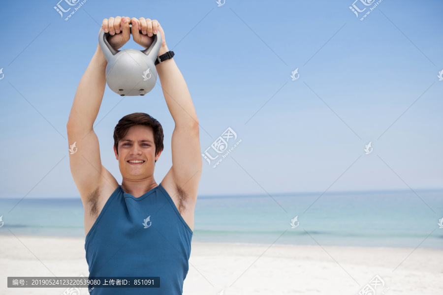 在海滩上拿着壶铃的年轻人