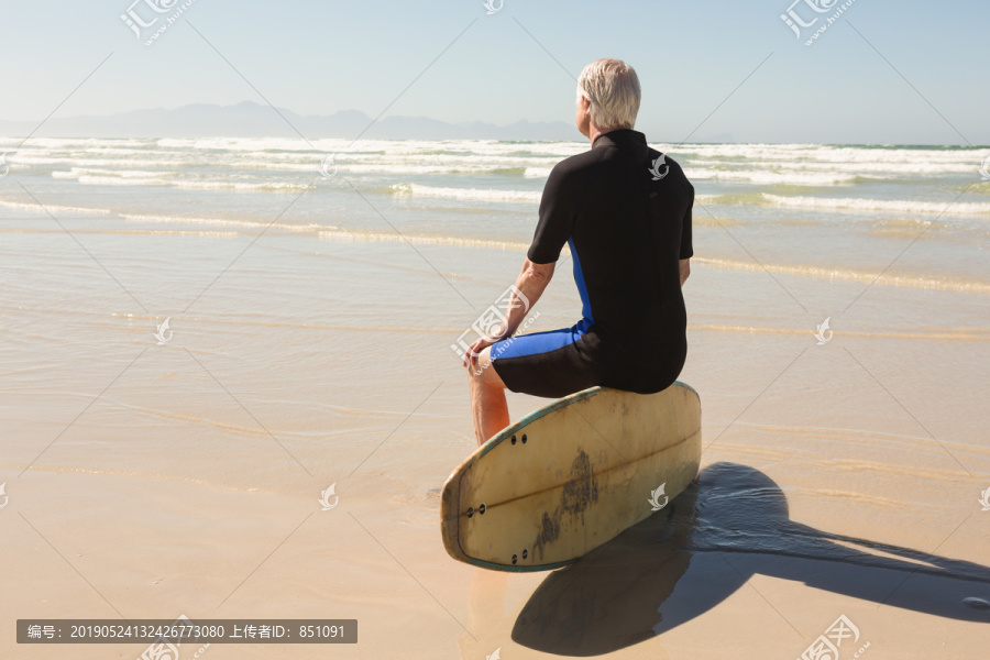 晴空下坐在冲浪板上的老人