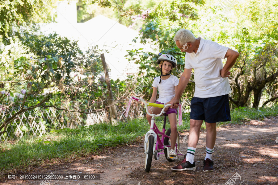 祖父和孙女在森林里练习自行车