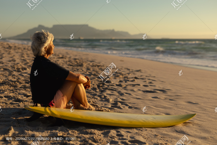 在海边拿着冲浪板的老太太