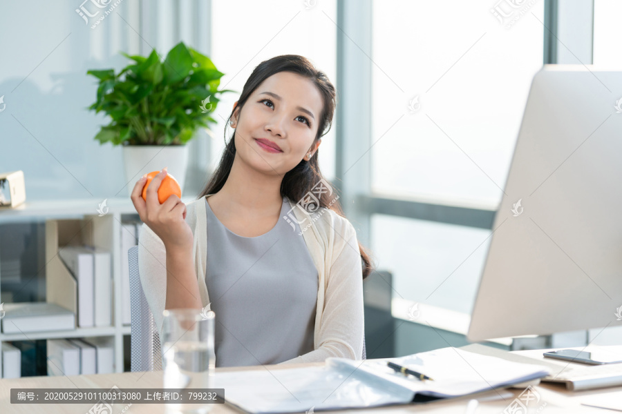 年轻女子在办公室拿着一个橙子