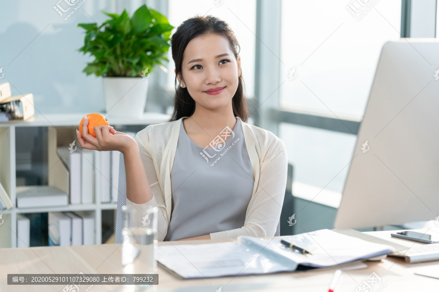 年轻女子在办公室拿着一个橙子
