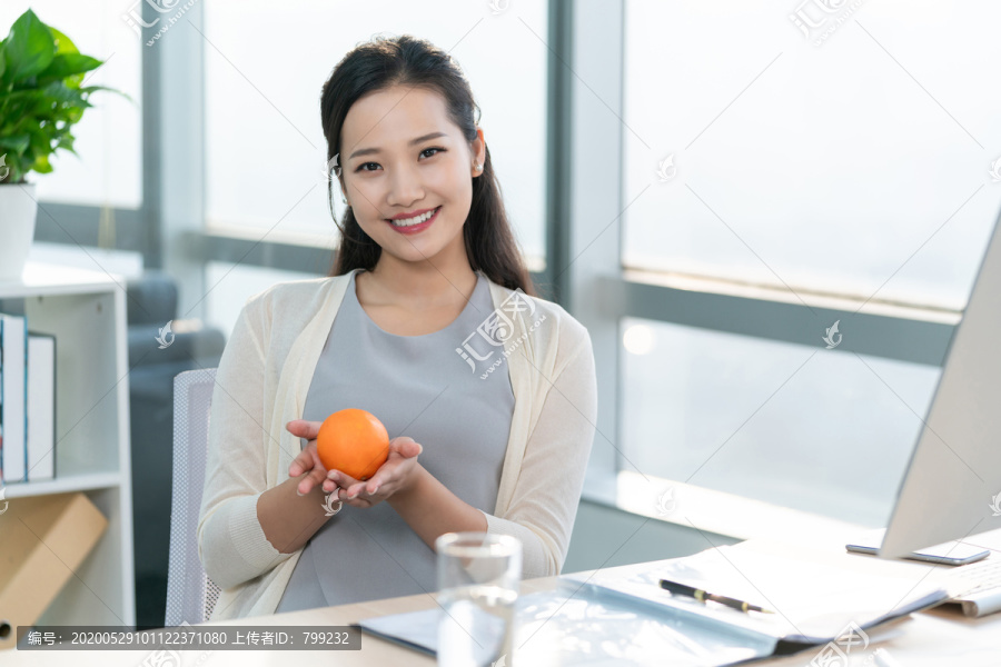 年轻女子在办公室拿着一个橙子