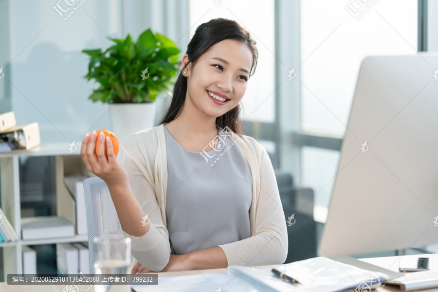 年轻女子在办公室拿着一个橙子