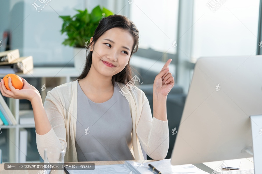 年轻女子在办公室拿着一个橙子