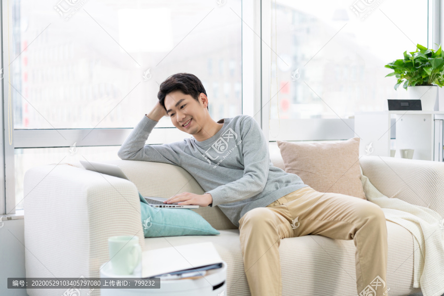 年轻男子在沙发上使用笔记本电脑