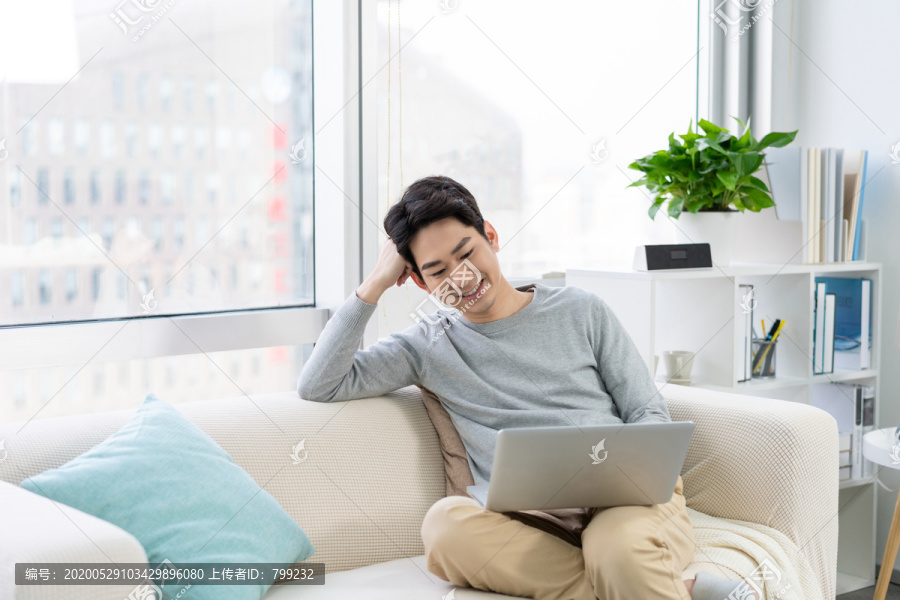 年轻男子在沙发上使用笔记本电脑