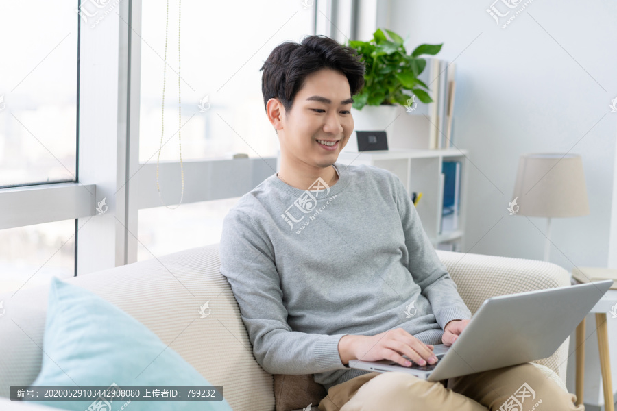 年轻男子在沙发上使用笔记本电脑
