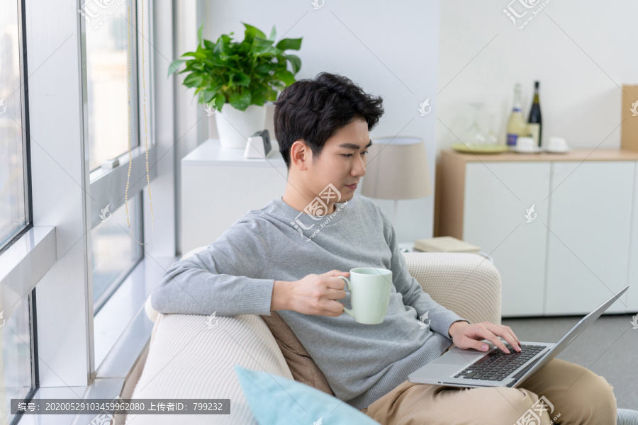 年轻男子在沙发上使用笔记本电脑
