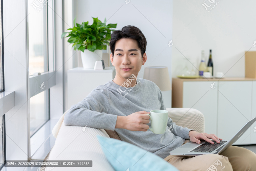 年轻男子在沙发上使用笔记本电脑