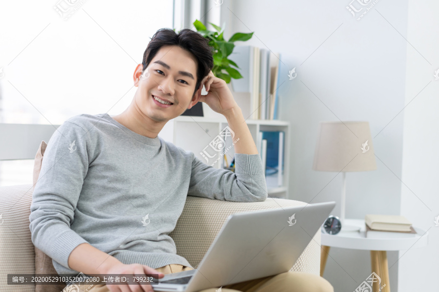 年轻男子在沙发上使用笔记本电脑