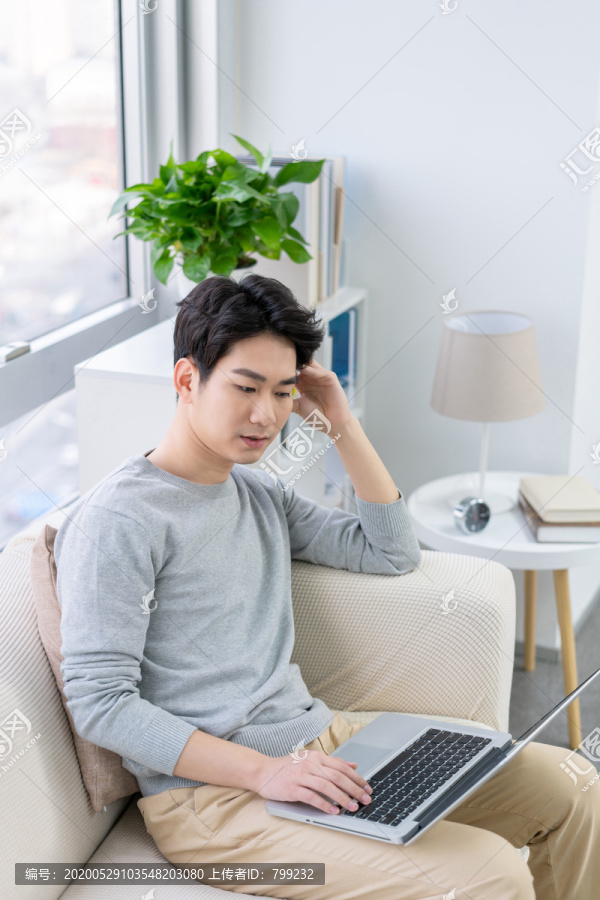 年轻男子在沙发上使用笔记本电脑