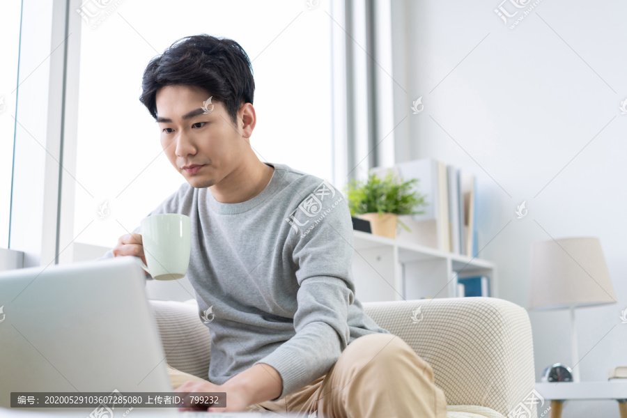年轻男子在沙发上使用笔记本电脑