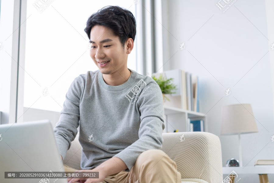 年轻男子在沙发上使用笔记本电脑