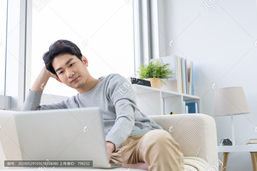 年轻男子在沙发上使用笔记本电脑