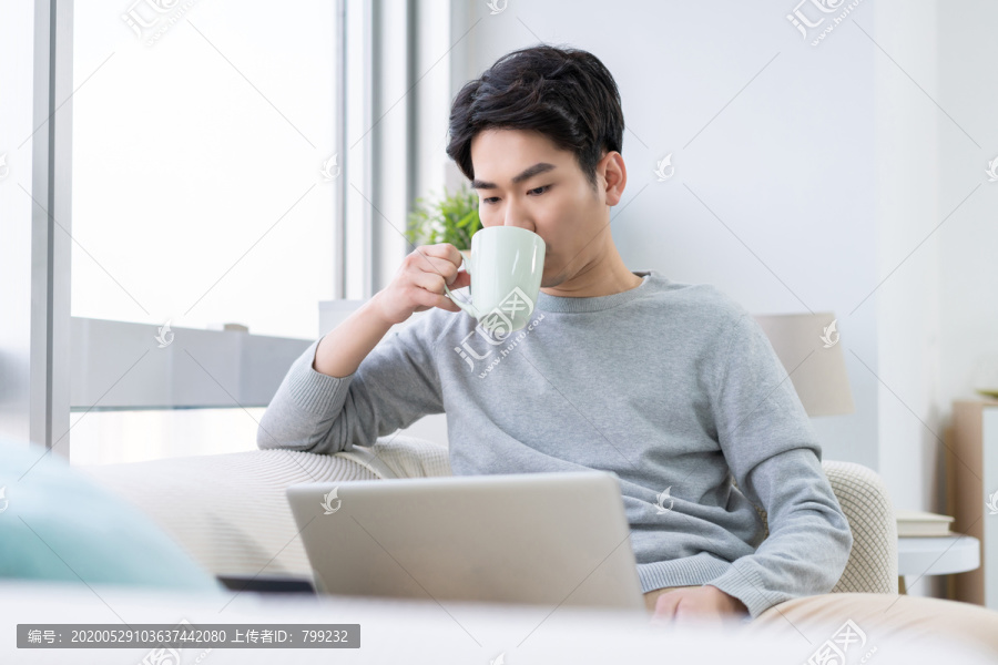 年轻男子在沙发上使用笔记本电脑