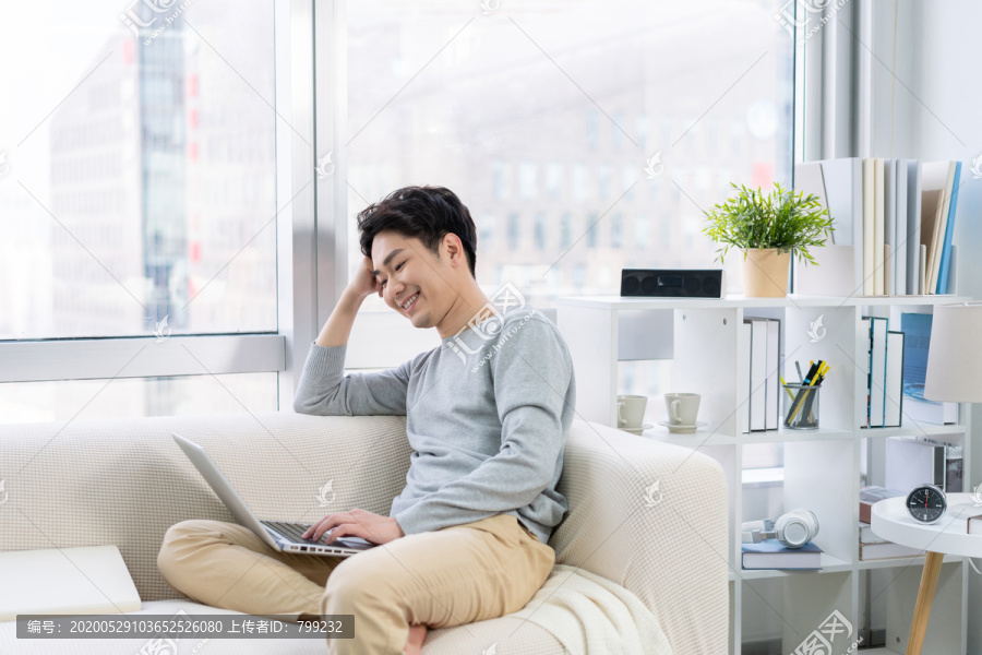 年轻男子在沙发上使用笔记本电脑
