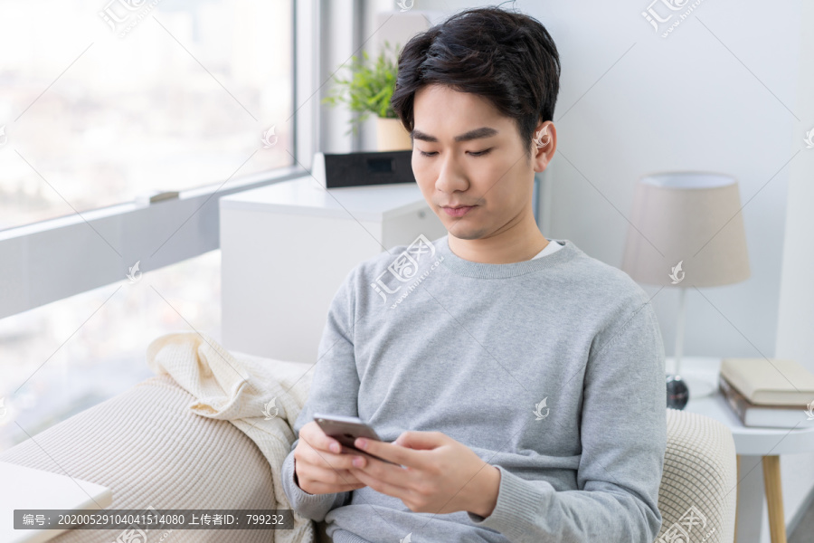 年轻男子坐在沙发上使用手机