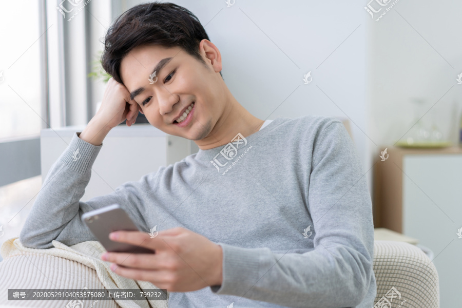 年轻男子坐在沙发上使用手机