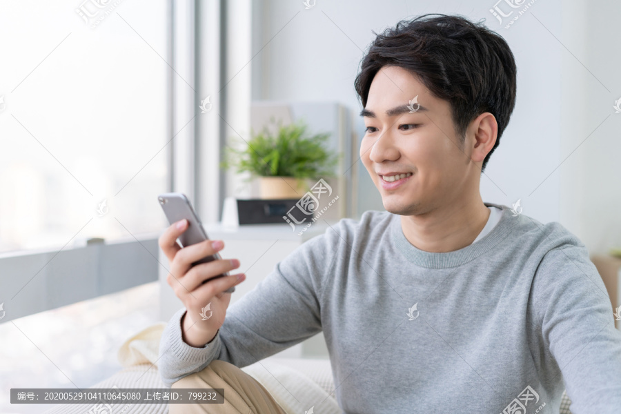 年轻男子坐在沙发上使用手机