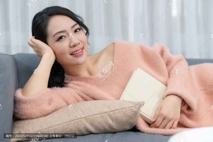 年轻女子躺在沙发上看书