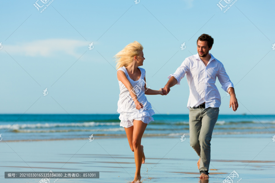 一对穿着白色衣服的情侣在沙滩上跑了下来，他们可能正在度假甚至度蜜月