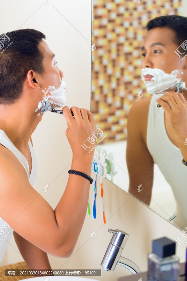 在浴室镜子前刮胡子的男性