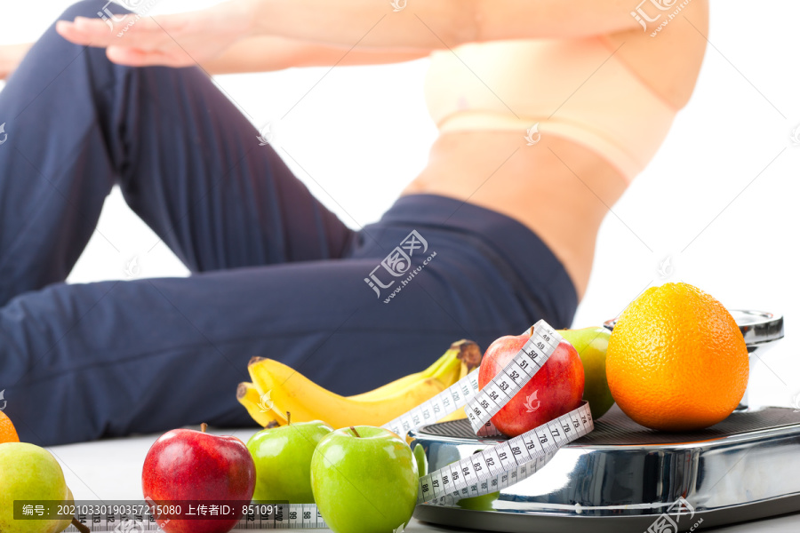 饮食和运动——年轻女子在一个磅秤、卷尺和水果旁做仰卧起坐