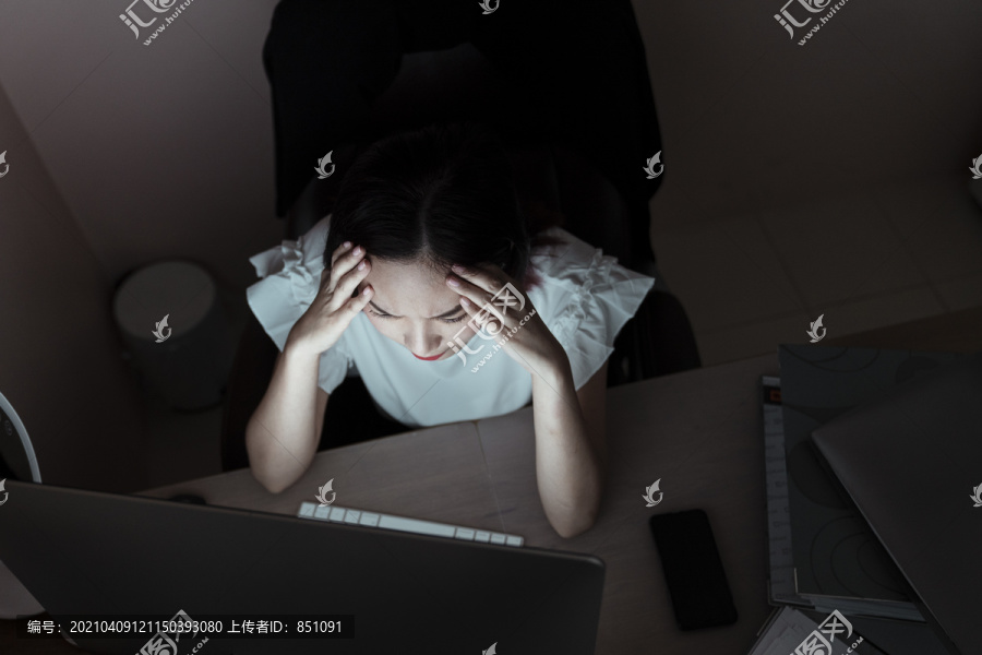 紧张的亚洲女商人在办公室对着电脑工作到午夜。