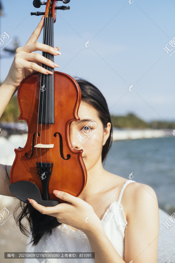 黑发白衣女子站在阳光下，把小提琴举到脸前。