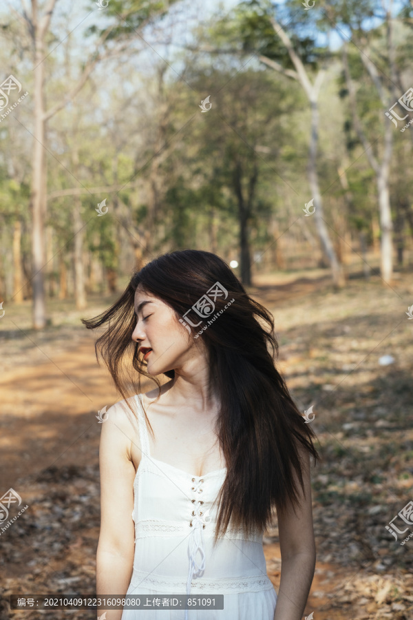 美丽的年轻女子穿着优雅的白裙在秋林中摇摇头。