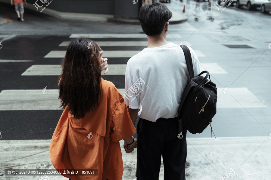 一对年轻夫妇一起走过斑马线，手牵着手的照片。