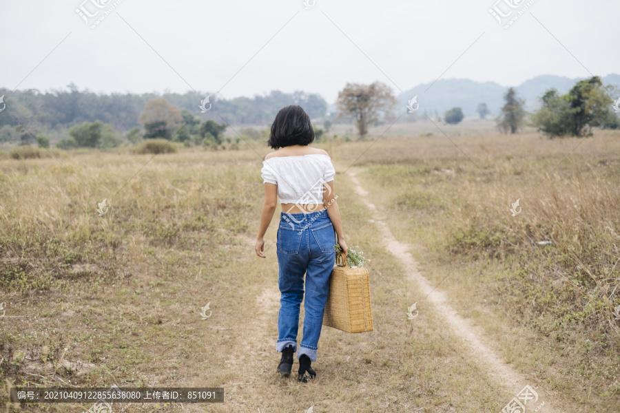 背景——来自首都的孤独女孩提着装满午餐的篮子走向田野。