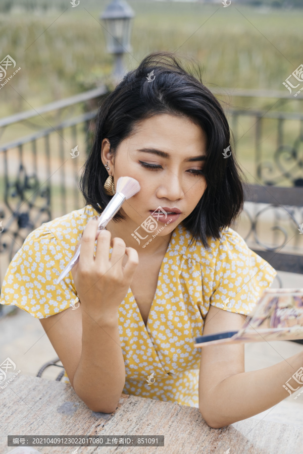 年轻的亚洲女人用刷子贴在脸上，坐在走廊外面。