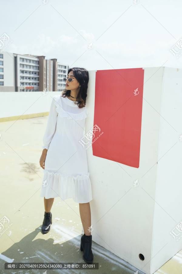 黑色卷曲长发的白裙女孩以别致的姿态站在白块红纸上。