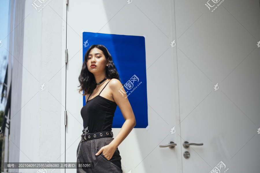 黑色卷曲长发女孩站在门前用蓝纸摆出别致的姿势。