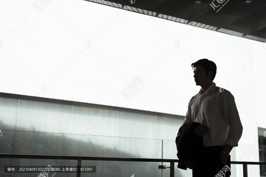 成熟的亚洲商人的剪影，穿着白色正式衬衫，手上挂着西装，背面有大屏幕的复印空间。