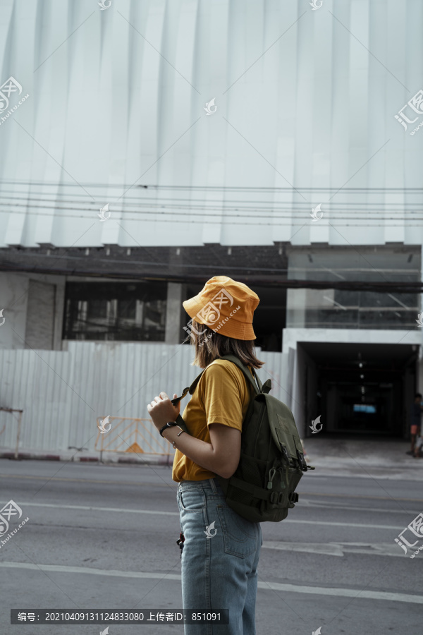 黄色背包女站在施工区前面，一边看一边背着绿色背包。