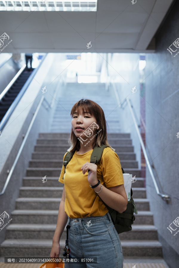 站在地铁站楼梯尽头的黄色背包女。