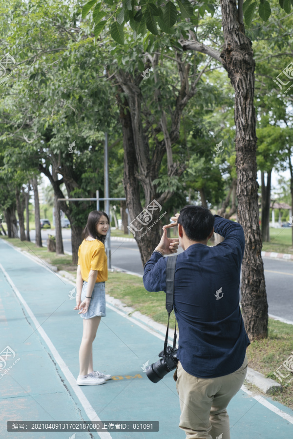 男摄影师在给一个女孩在自行车道上拍照前用手定格。