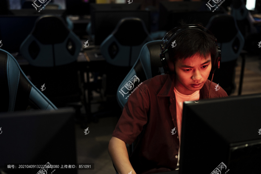 愤怒的亚洲玩家在输掉比赛后变得严肃起来。红色霓虹灯下网吧的电脑游戏玩家。